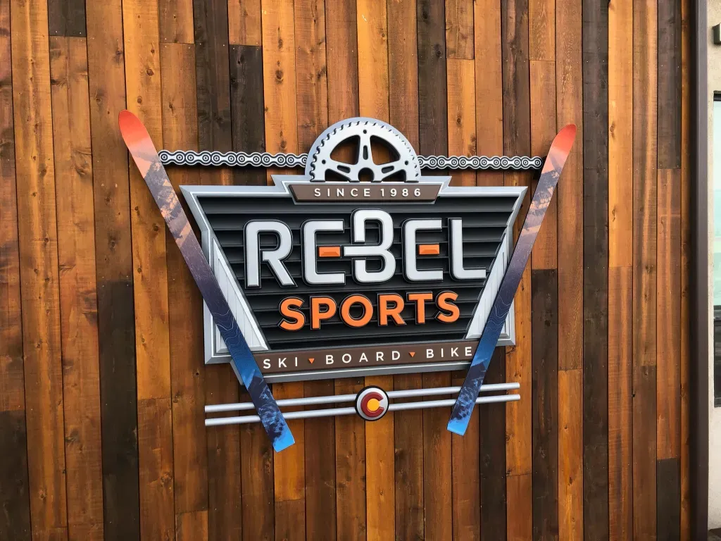 An elaborate sign the says rebel sports installed on stained wood stud wall.